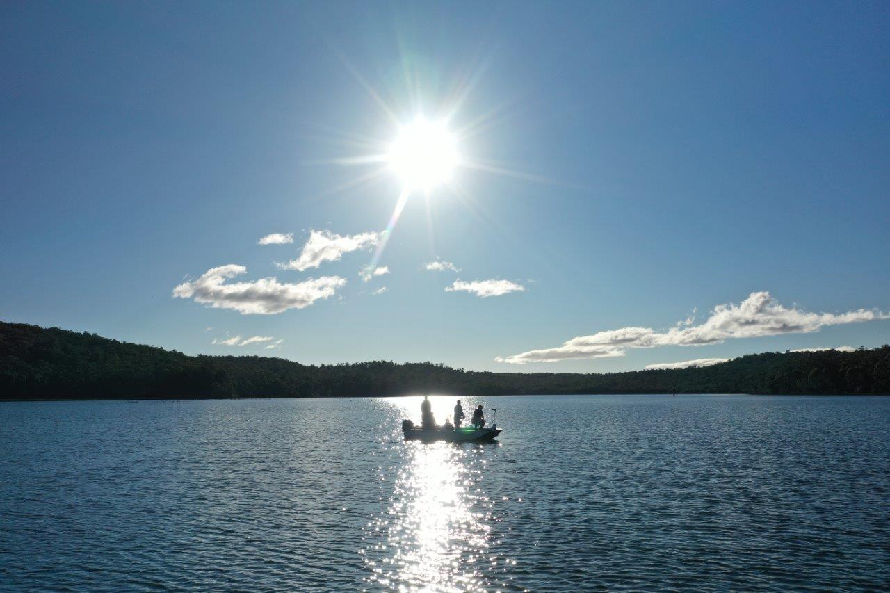 Anglers in a boat on a lake with the sun reflecting on the water