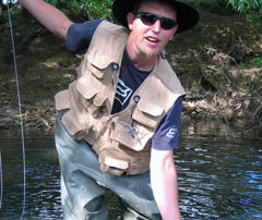 Brian holds a wild brown trout in his left hand and his rod up high in his right hand on the St Patrick's River Tasmania